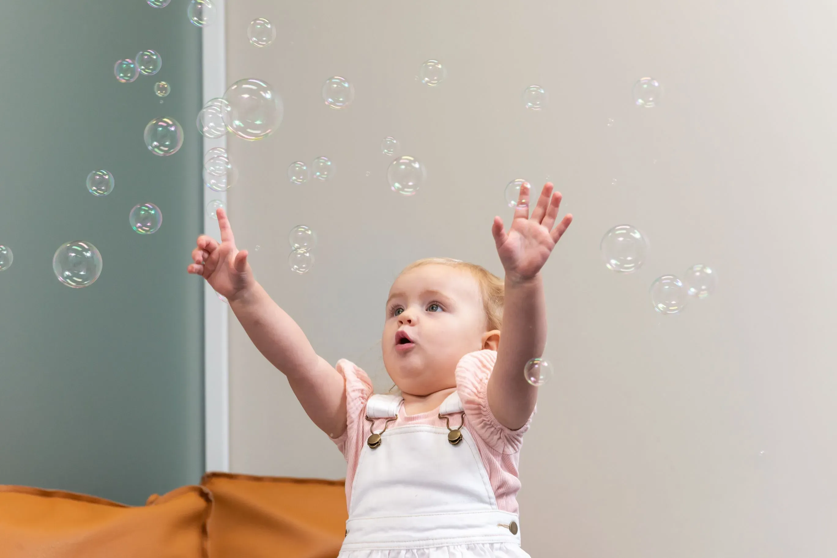 A child looking up inquisitively at some bubbles that have been blown and are floating around them.